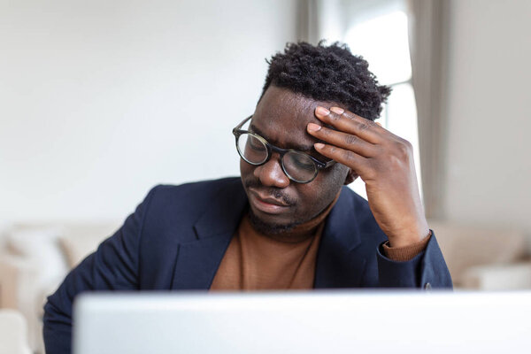 Stressed tired African American man touching temples, suffering from headache after long hours work, overworked overwhelmed businessman sitting at desk, feeling unwell