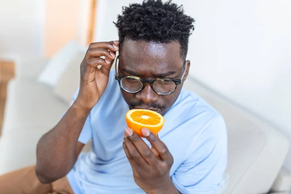 Sick Arican man trying to sense smell of half fresh orange, has symptoms of Covid-19, corona virus infection - loss of smell and taste. One of the main signs of the disease.