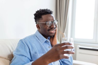 Hassas dişleri ve bir bardak buzlu soğuk suyu tutan genç adam. Sağlık sigortası konsepti. Soğuk içecek içen bir adam, buzla dolu bir bardak ve diş ağrısı hisseden bir adam.