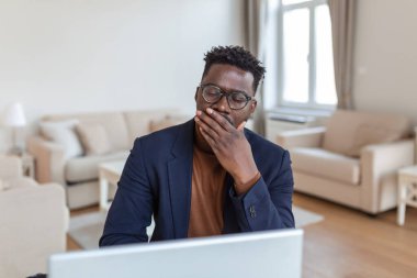 Yorgun adam uzun bir iş gününden sonra esniyor. Sabahın köründe çalışıyorum. Uykulu yorgun serbest çalışan, evinde dizüstü bilgisayarın ekranının önünde esniyor.