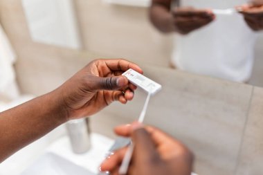 Genç Afrikalı Amerikalı adam evde antijen kiti ile COVID-19 testi yaptırıyor. Coronavirus enfeksiyonunu kontrol etmek için burun sopasıyla giriyoruz. Karantina, salgın hastalık.