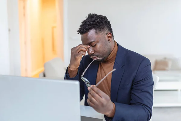 Tired African American businessman taking off glasses, exhausted employee massaging nose bridge, suffering from eye strain after long computer work, feeling pain, health problem concept