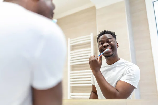 歯ブラシ洗浄とバスルームで鏡を見てアフリカ人の男を笑顔 バスルームで朝歯を磨くハンサムな若い男 ハッピー男でパジャマブラッシング歯夜寝る前に — ストック写真