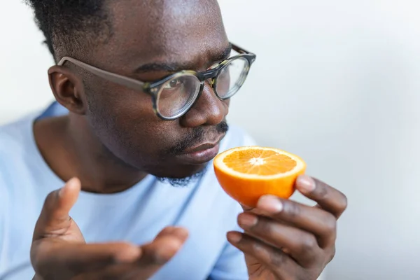 Sick Arican man trying to sense smell of half fresh orange, has symptoms of Covid-19, corona virus infection - loss of smell and taste. One of the main signs of the disease.