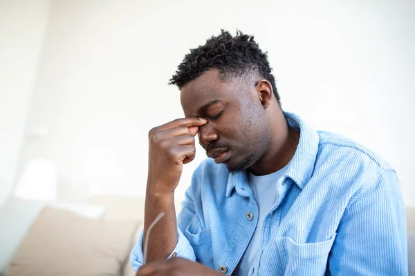 Tired African American man taking off glasses, exhausted massaging nose bridge, suffering from eye strain after long computer work, feeling pain, health problem concept