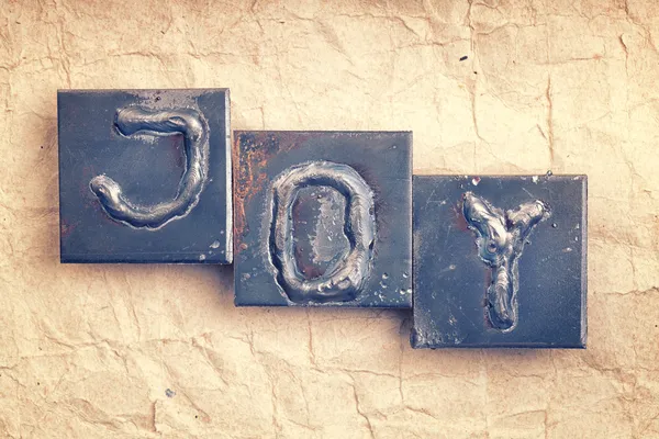 La parola "JOY" fatta da lettere in metallo su una vecchia carta vintage b — Foto Stock