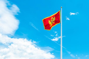 Arkaplanda mavi bulutlu gökyüzü bulunan Karadağ Ulusal Bayrağı 