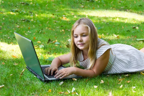 Nettes Mädchen mit Laptop auf grünem Gras — Stockfoto