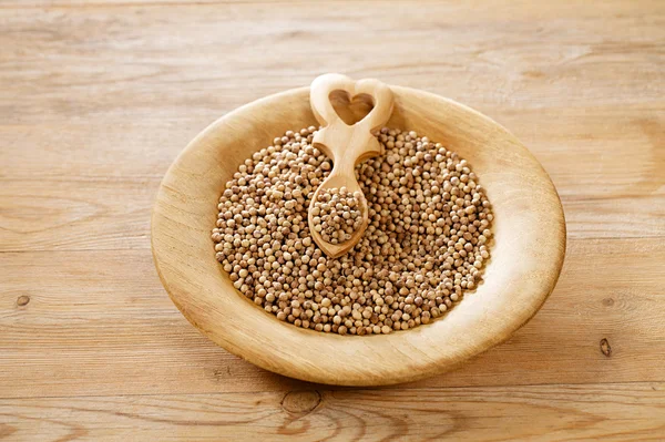White coriander seeds in wooden plate with heart shaped spoon — Stock Photo, Image