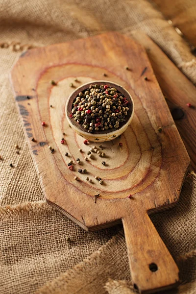 Mixed pepper, pink, black, white, green in bowl on wooden boar — Stock Photo, Image