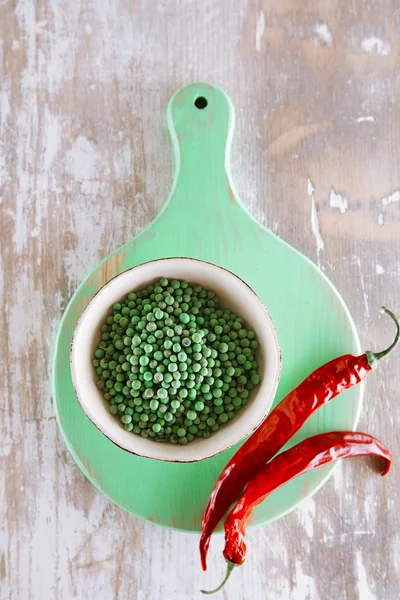 Green peppercorns in bowl and red chillies on green wooden board — Stock Photo, Image