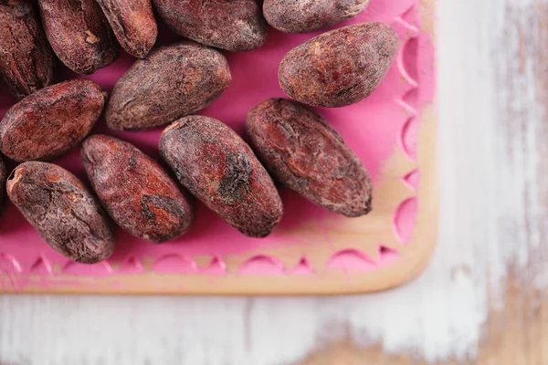 粉红和白色的木背景上烤可可巧克力豆 — 图库照片