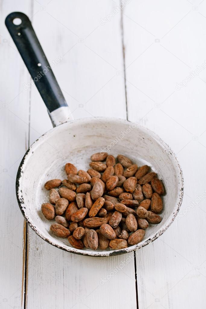 Roasted cocoa chocolate beans in pan on white wood background