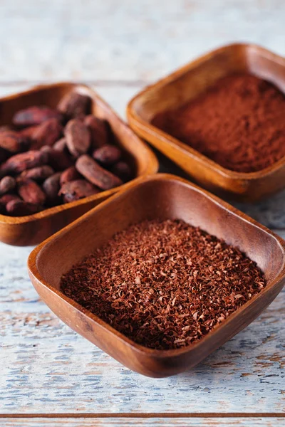 Cacaobonen, poeder en geraspte chocolade in houten kommen, wit — Stockfoto