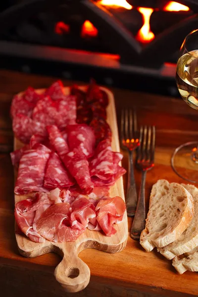 Platter of serrano jamon Cured Meat with cozy fireplace and wine — Stock Photo, Image