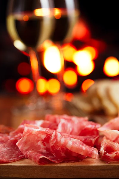 Platter of serrano jamon Cured Meat with cozy fireplace and wine — Stock Photo, Image