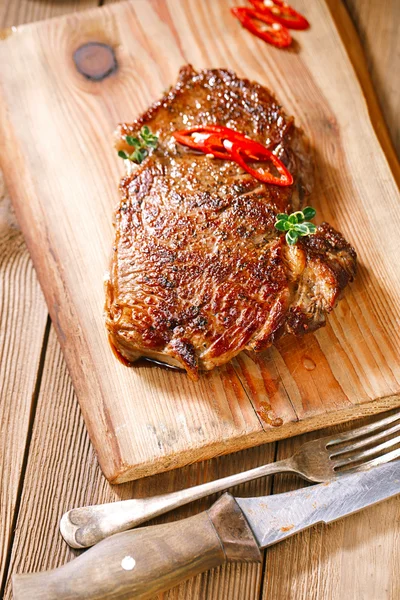 Beef steak with red chillies on wood and table — Stock Photo, Image