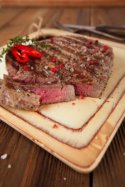 Bife de carne em uma tábua de madeira e mesa — Fotografia de Stock