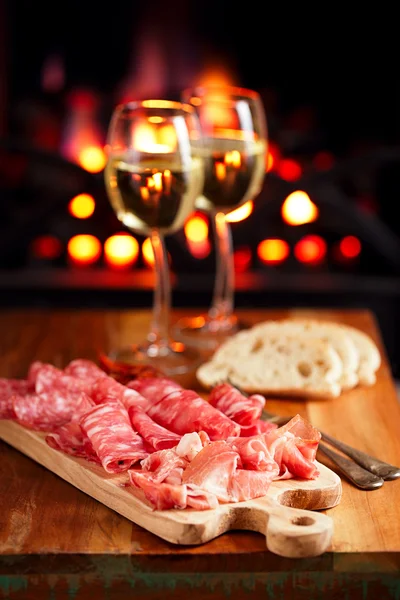 Platter of serrano jamon Cured Meat with cozy fireplace and wine — Stock Photo, Image