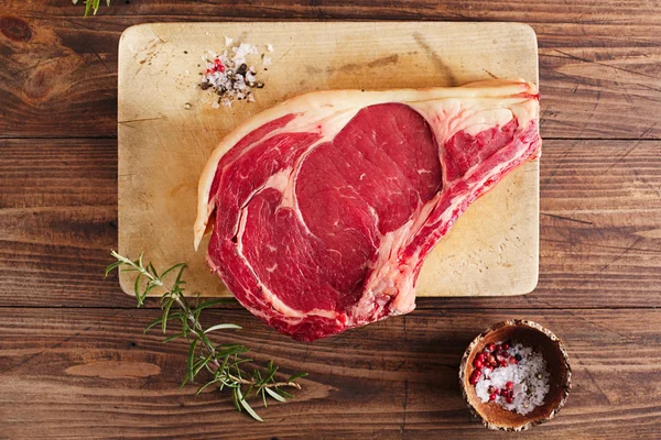 Carne crua costela osso bife na tábua de madeira e mesa — Fotografia de Stock