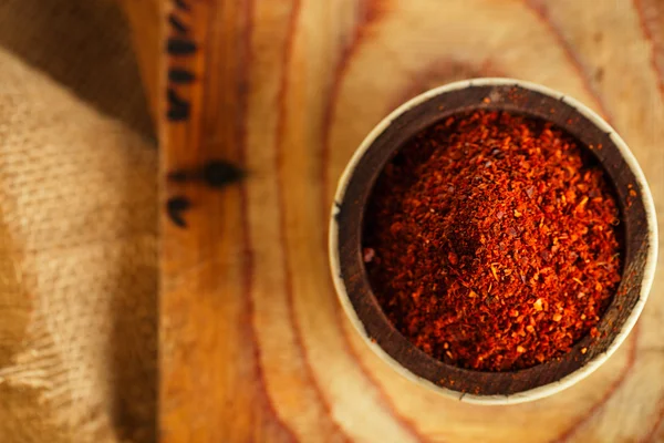 Red hot chillies pepper flakes in bowl on wooden board backgro — Stock Photo, Image