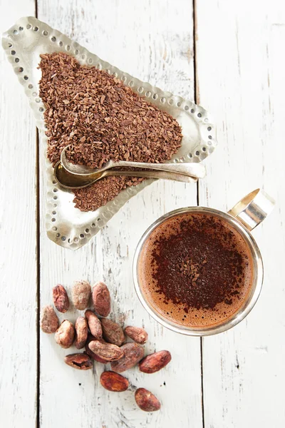 Chocolate caliente, granos de cacao y chocolate rallado en madera blanca — Foto de Stock