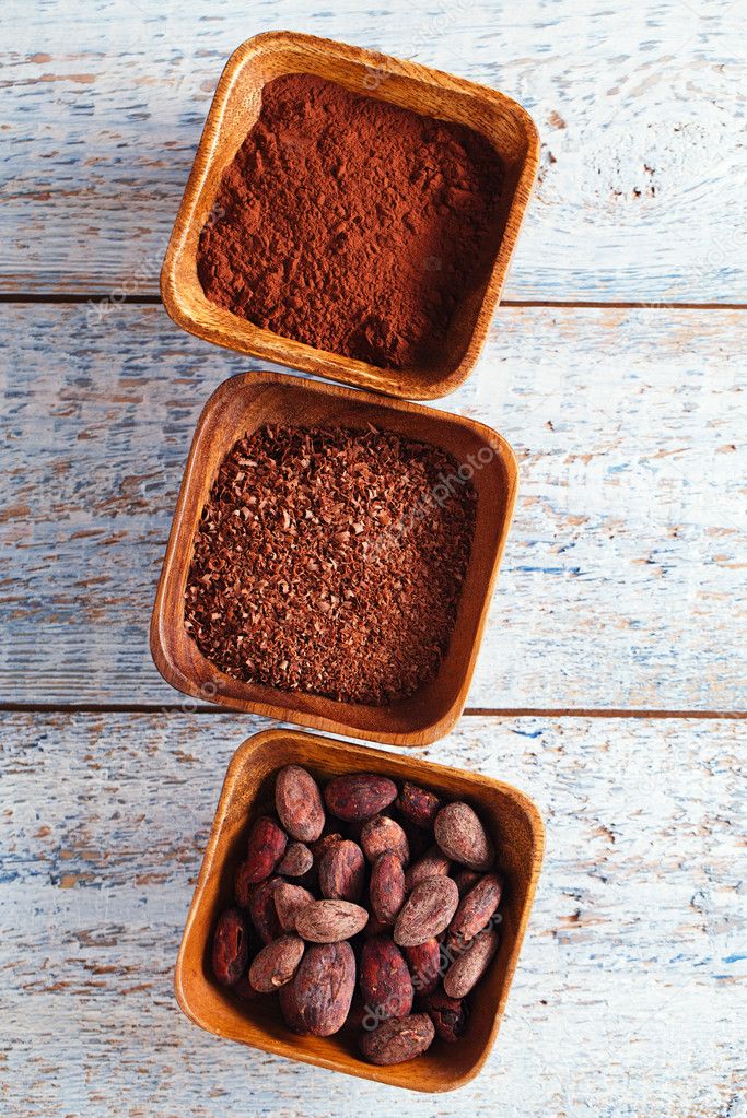 cocoa beans, powder and grated chocolate in wooden bowls, white