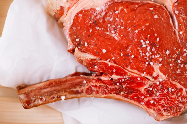 Bone-in Rib eye Filete de filete sobre papel y mesa de madera — Foto de Stock