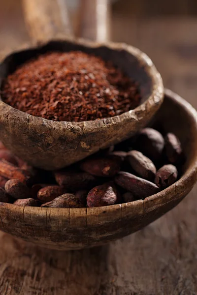 Cocoa beans and grated dark chocolate in old texured spoons bowl — Stock Photo, Image