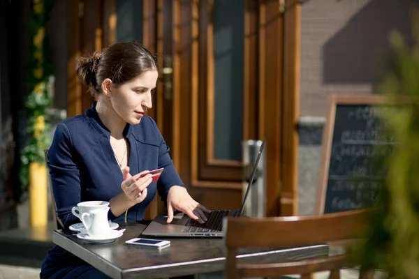 Mujer de negocios con tarjeta de crédito y portátil sentado en una mesa en —  Fotos de Stock