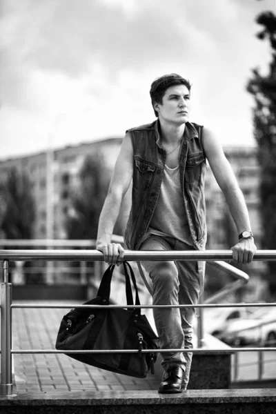 Black and white photo of the fashion guy with a bag standing in — Stock Photo, Image