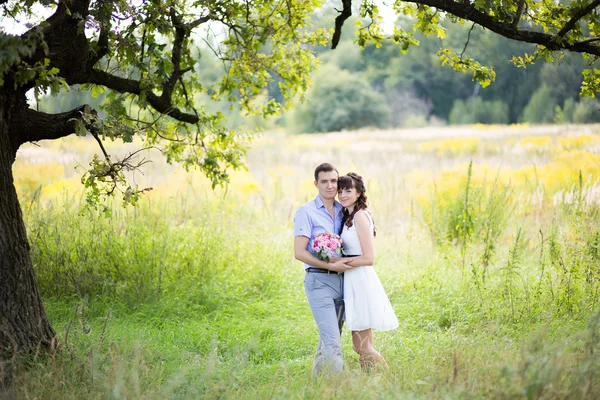 Man and woman standing in the grass under a tree on a background — Stock Photo, Image