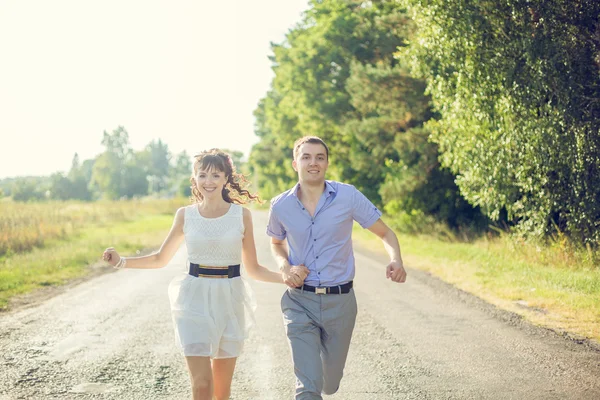 Girl with a guy running down the road holding hands — Stock Photo, Image