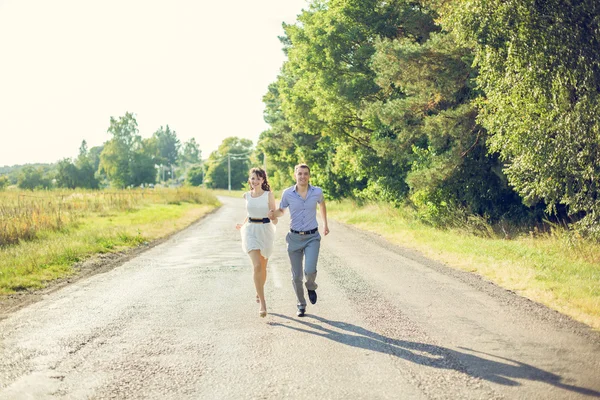 Girl with a guy running down the road holding hands — Stock Photo, Image