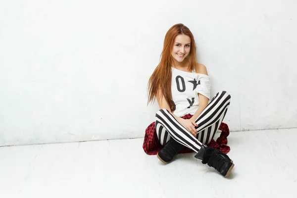 Giovane, ragazza elegante posa seduta su un pavimento bianco contro un wh — Foto Stock