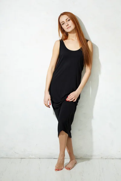 Skinny girl with long legs in black dress standing on a white fl — Stock Photo, Image