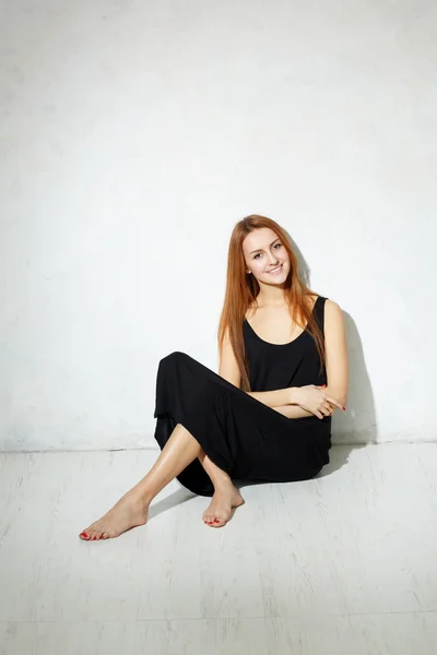 Magra ragazza con le gambe lunghe in abito nero seduto su un flo bianco — Foto Stock