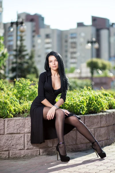 Sexy menina vestido preto sentado na rua, no fundo o — Fotografia de Stock