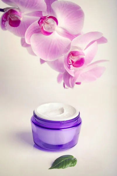 Face, hand cream jar and purple orchid flowers, vertical shot — Stock Photo, Image