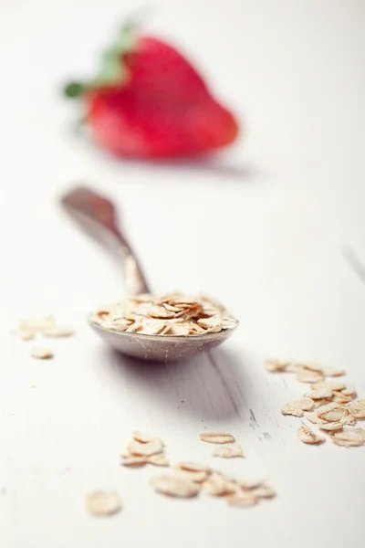 Oat flakes in an old spoon and a strwberry on wooden table, tone — Stock Photo, Image
