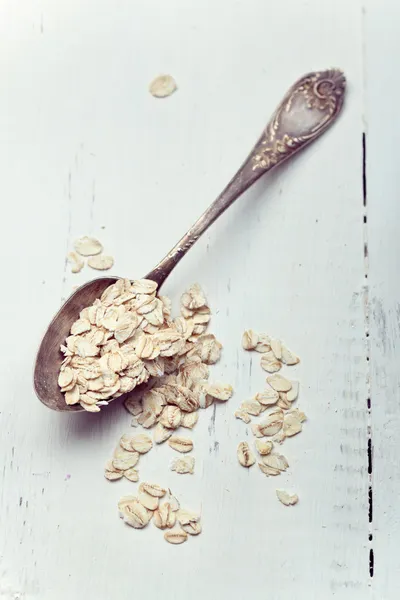 Copos de avena en una cuchara vieja sobre mesa de madera, foto tonificada —  Fotos de Stock