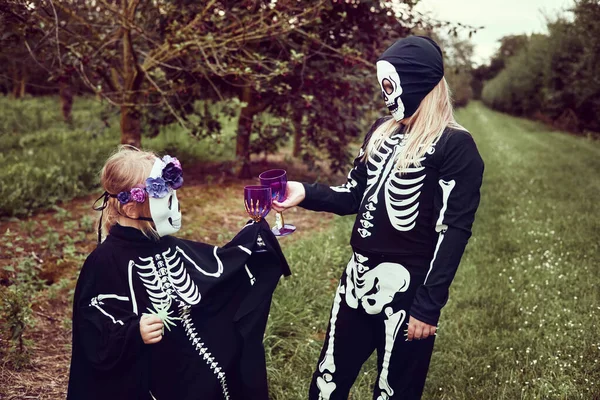 Dos hermanas disfrazadas de esqueleto y bruja divirtiéndose en la fiesta de Halloween y haciendo truco o trato al aire libre —  Fotos de Stock