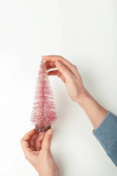 Primo piano di mani di donne che tengono un piccolo albero di Natale decorativo luccicante rosa, flatlay — Foto Stock