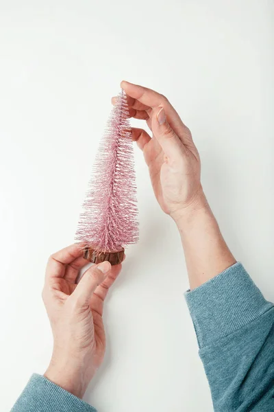 Fechar-se de umas mãos de mulher que mantêm uma pequena árvore de Natal decorativa cintilante rosa, flatlay Imagens Royalty-Free