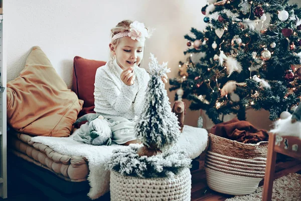 Bambina - bambino - che gioca con giocattoli e decorazioni seduti accanto a un albero di Natale Fotografia Stock