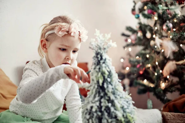 Liten jente - småbarn - leker med leker og pynt ved siden av et juletre stockbilde