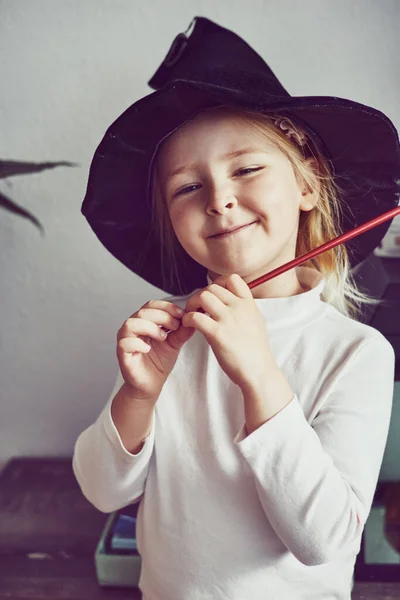 어린 소녀는 집에서 마법 모자를 쓰고 상상력 있는 마법사 놀이를 하고 있습니다. 주문을 외워 로열티 프리 스톡 이미지