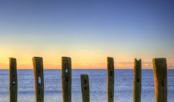 Oude groynes op de laatste Defensie strand bij zonsopgang tegen tij — Stockfoto