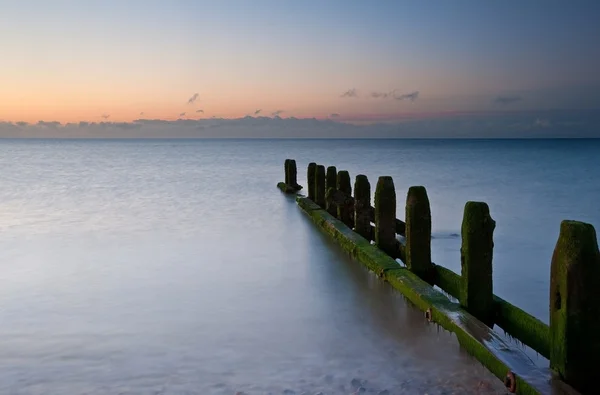 日の出に対する最後の防衛はビーチに古い groynes 潮します。 — ストック写真