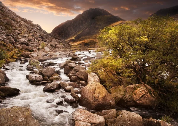 Waterfall in mountains with moody dramatic mountain sunset lands
